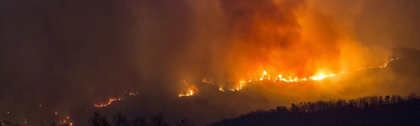 A wildfire burning along a dark ridge.