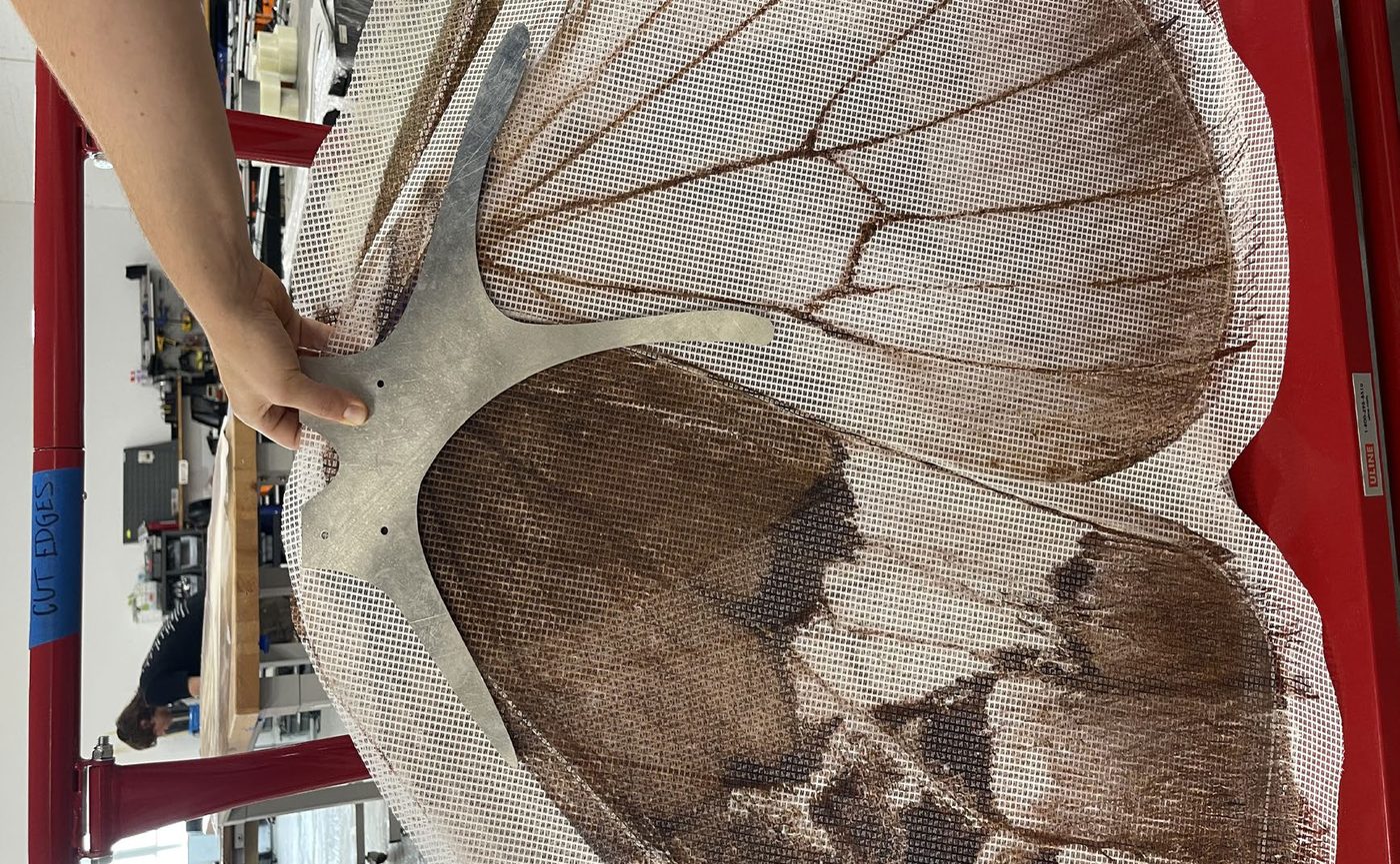 A hand smoothing UV-printed mesh over a wing form.